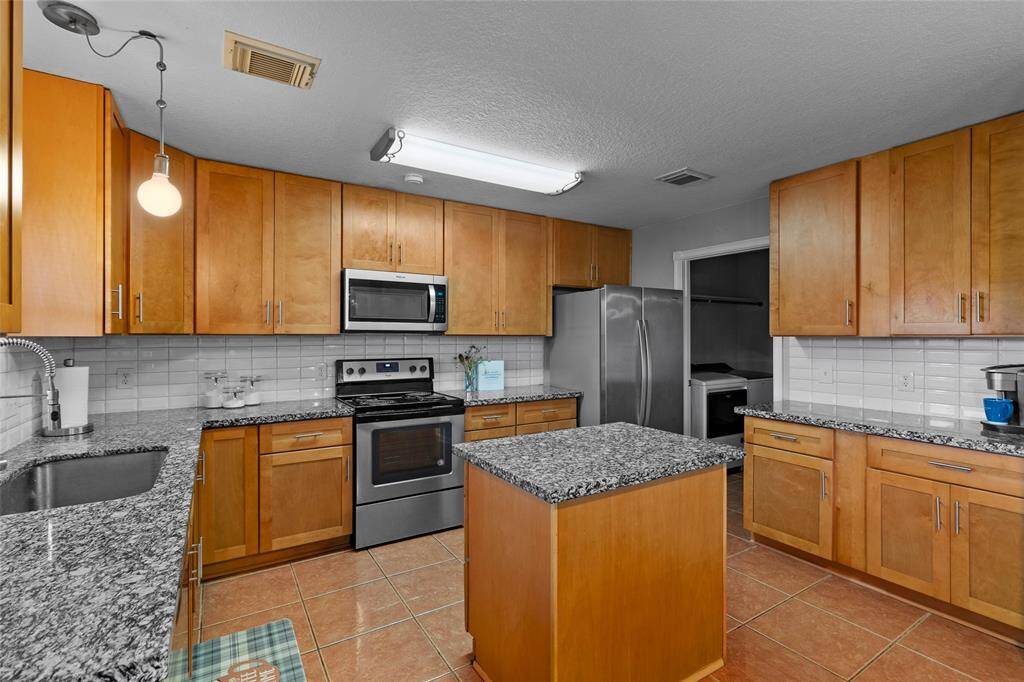 Your kitchen features a central island for added counter space and versatility. Ample cabinetry ensures organized storage, while stainless steel appliances bring a sleek, modern touch. A stylish tile backsplash enhances the design, offering both visual appeal and easy maintenance in this functional and inviting space.