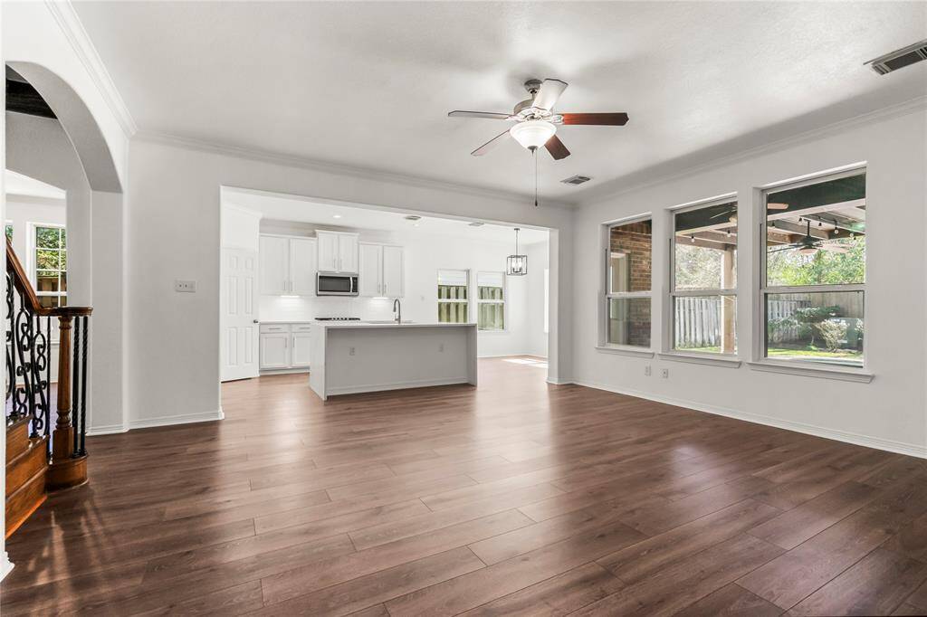 This photo showcases a spacious open-concept living area with vinyl floors, a modern kitchen with white cabinetry and an island, and large windows providing natural light and a view of the pool area.