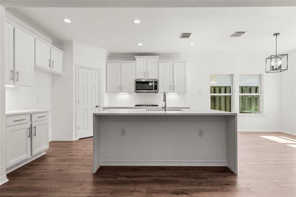 This modern kitchen features sleek white cabinetry, a central island with a built-in sink, and stainless steel appliances.