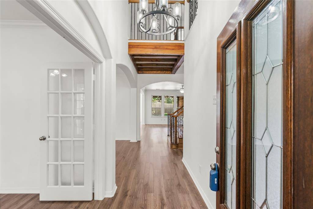 This photo showcases a bright entryway with elegant wooden flooring and ornate glass doors. The hallway leads to an open living area with large windows, highlighting the home's spacious and inviting design. A stylish staircase with wrought iron railings adds a touch of sophistication.