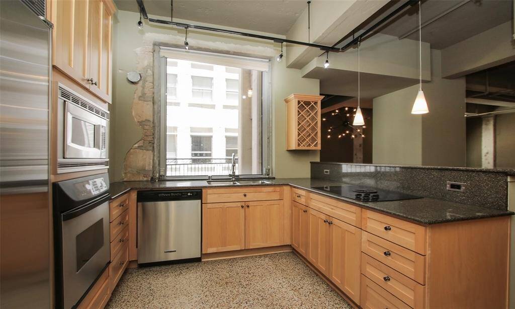 Designer kitchen features Terrazzo floors, wood cabinetry, granite counters and backsplash, pendant & track lighting, KitchenAid stainless steel appliances built-in wine shelf, and breakfast bar.