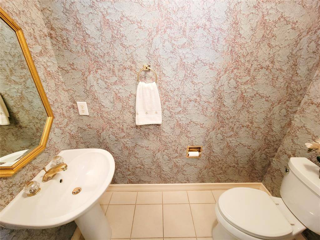 Quaint Powder Room off hallway leading to primary bedroom, pedestal sink, elevated toilet, rich wallpaper, brushed gold accents