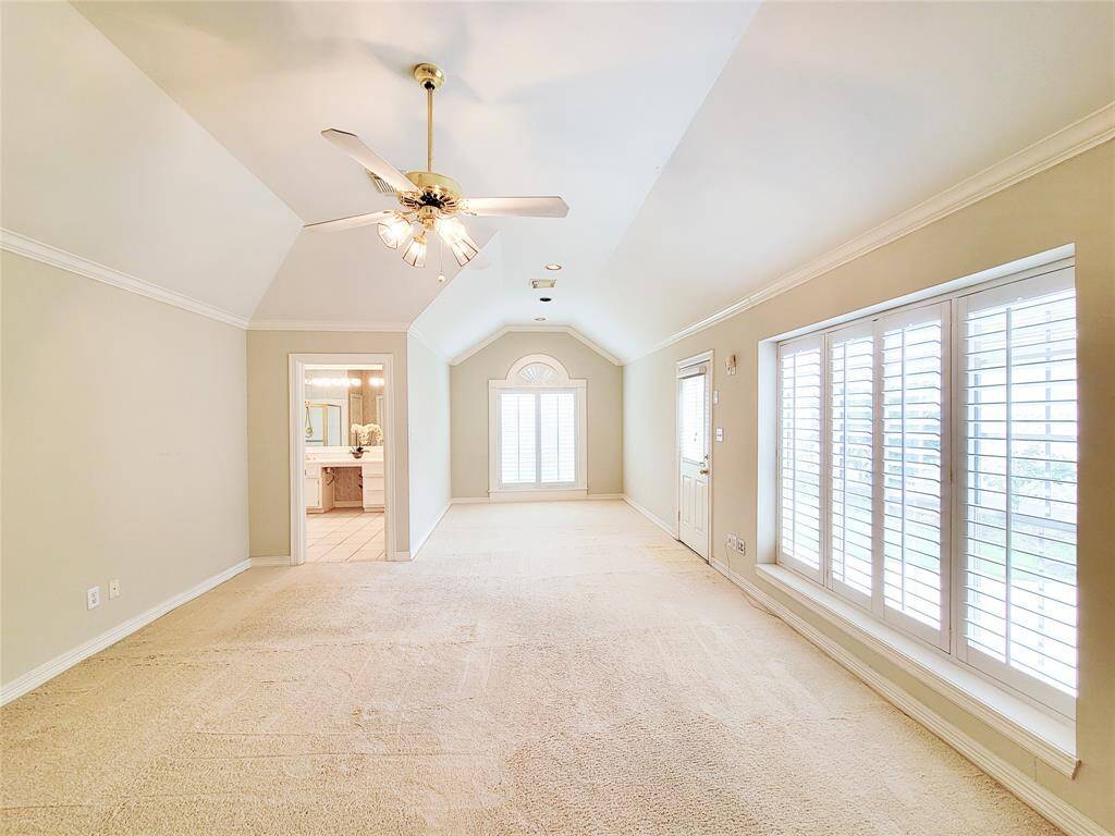 large Primary Bedroom-wall of windows with plantation shutters overlooking backyard & patio door. En-suite bath at back left, crown molding, detailed ceiling.
