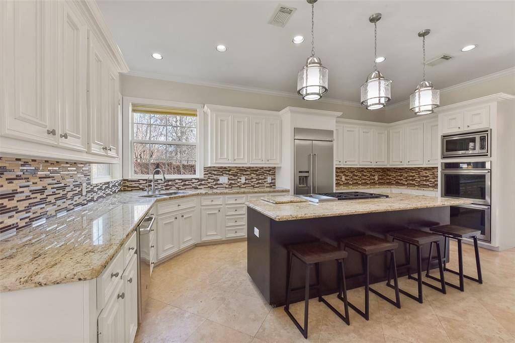 CHEF’S KITCHEN FEATURING A MASSIVE ISLAND, GRANITE COUNTERTOPS, CUSTOM CABINETRY, AND HIGH-END STAINLESS STEEL APPLIANCES.