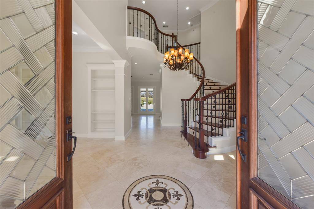 DRAMATIC ENTRYWAY FEATURING A SWEEPING CURVED STAIRCASE AND ELEGANT CHANDELIER.