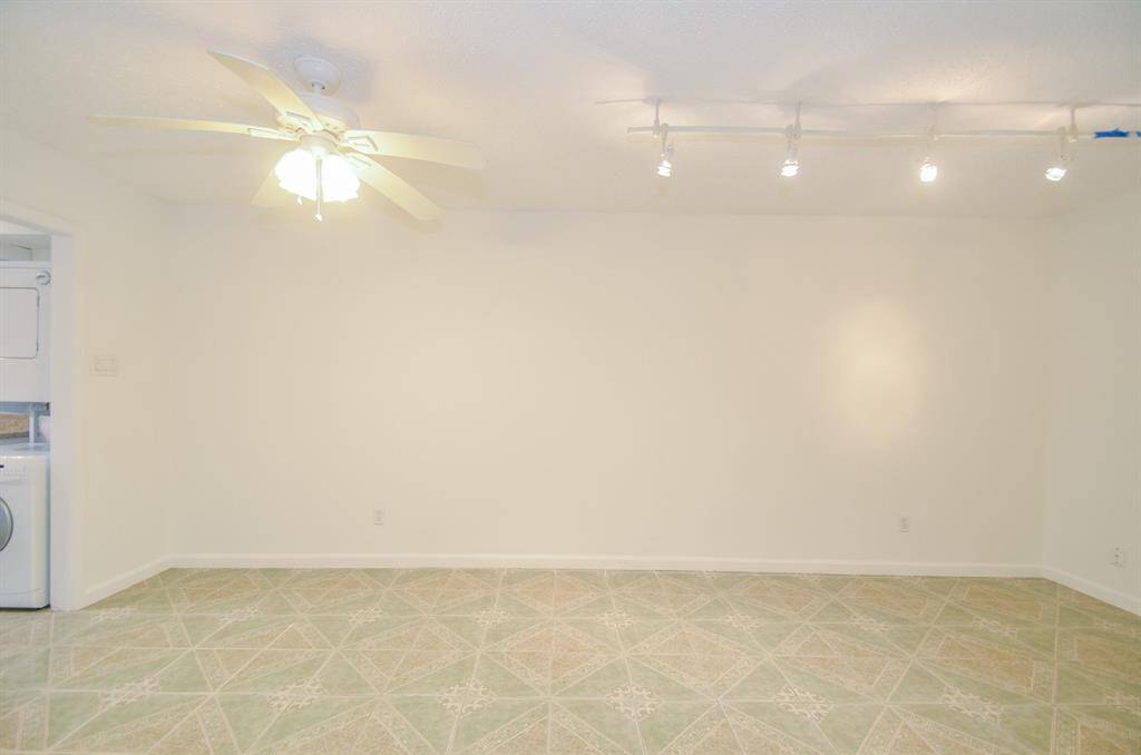 Bright room with neutral walls and patterned flooring, featuring a ceiling fan and track lighting. There's a laundry area visible through an open doorway.