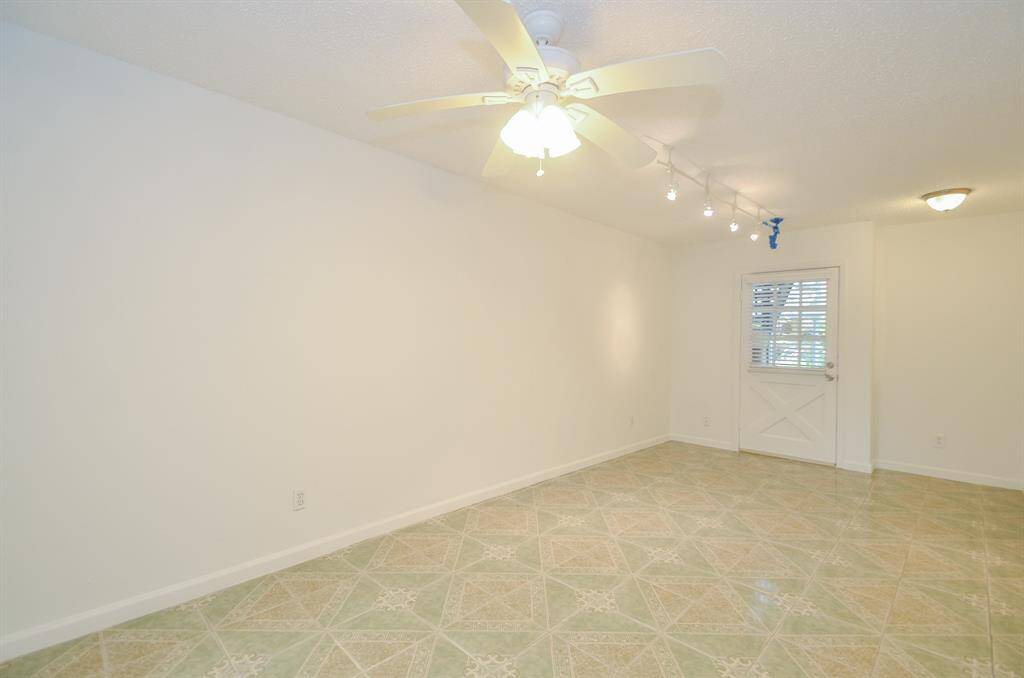 This bright room features a ceiling fan and track lighting, with light-colored tiled flooring and neutral walls. A window and door provide natural light and outdoor access, creating an inviting and versatile space.