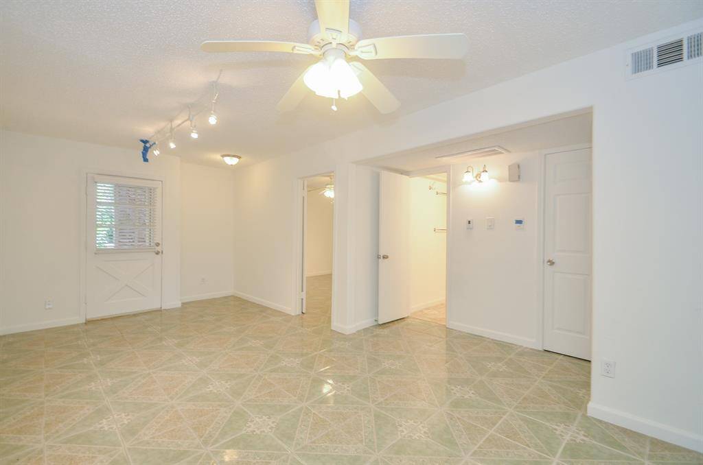 Bright room with tiled floors and neutral walls, featuring a ceiling fan and track lighting. It includes a door with a window, a small adjacent area, and two open doorways leading to other spaces.