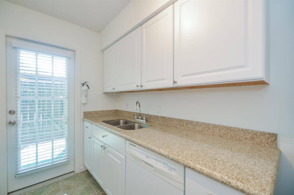 Bright laundry room with ample storage, featuring white cabinets and granite countertops. Includes a stainless steel sink and a door with glass panels for natural light.
