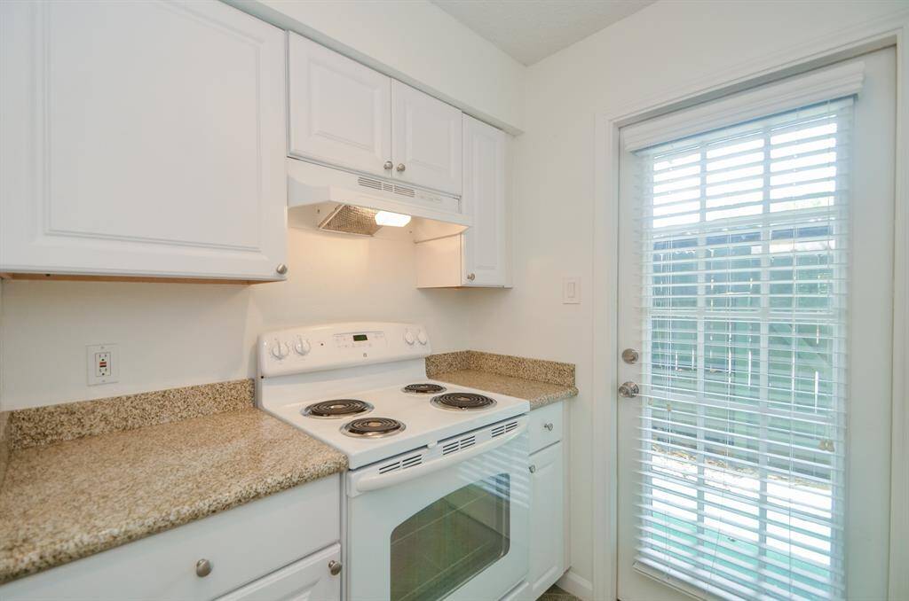 This kitchen features white cabinetry, granite countertops, and a white electric stove. It has a door with glass panes leading outside, allowing natural light to brighten the space.