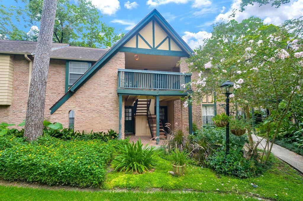 This photo showcases a charming two-story home with a brick exterior and a quaint balcony. It's surrounded by lush greenery and mature trees, offering a serene and inviting atmosphere. The architectural details add character, making it an appealing choice for home buyers seeking a cozy and picturesque setting.