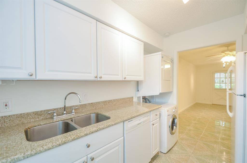 Bright kitchen with granite countertops, double sink, white cabinetry, and in-unit washer/dryer. It opens to a dining area with tile flooring and a ceiling fan.