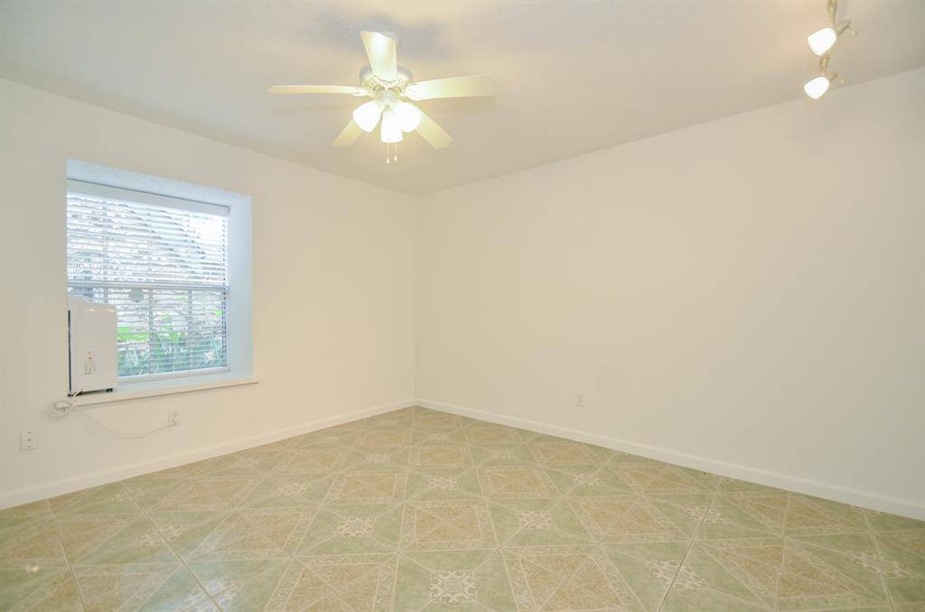 This bright room features tiled flooring, a ceiling fan, and ample natural light from a large window with blinds, creating a cozy and inviting space.