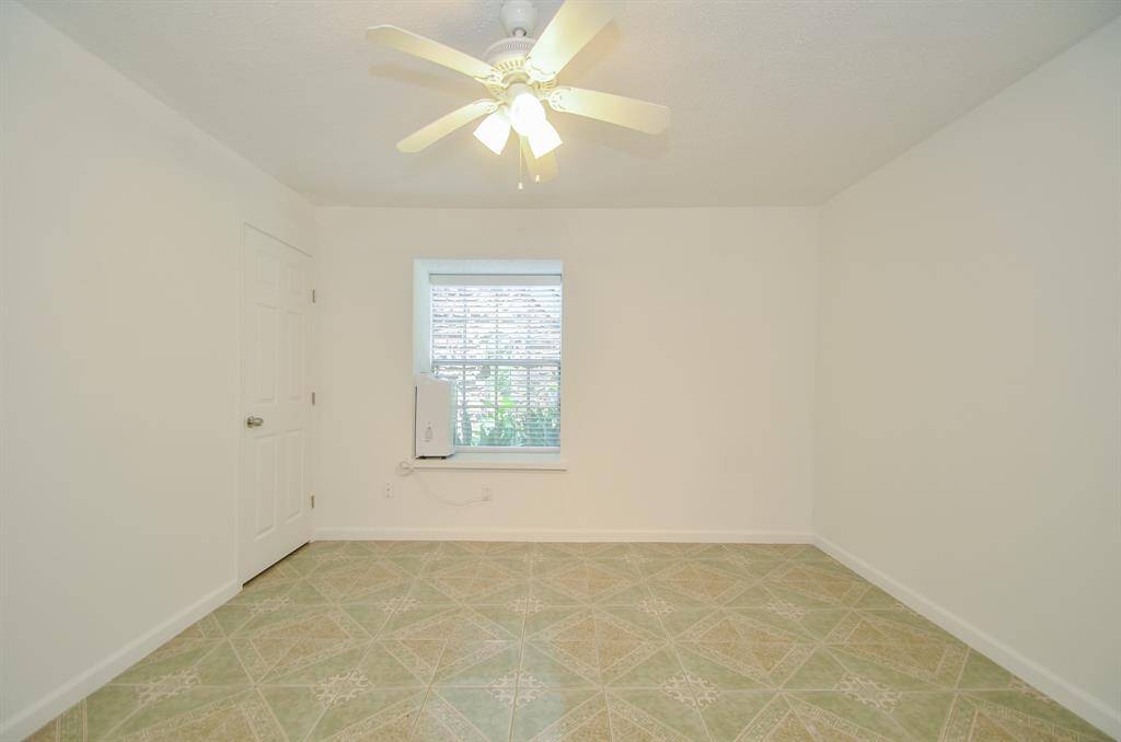 This room features neutral walls, a ceiling fan, and a window allowing natural light. The floor has decorative tiles, and there's a door to one side, creating a bright and functional space.