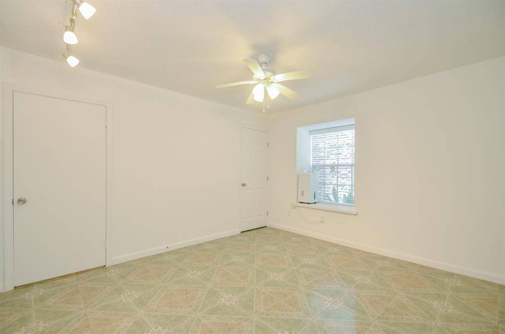 Bright room with neutral walls and tiled flooring. Features a window with natural light, a ceiling fan, and track lighting. Simple and versatile space.