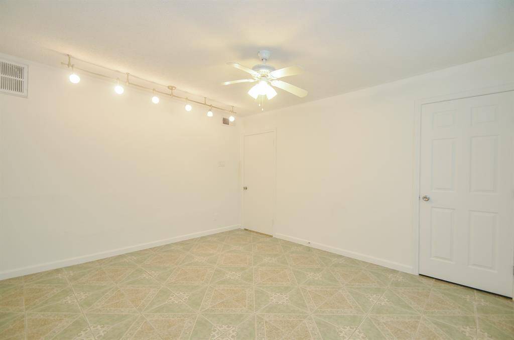 This room features neutral walls, a ceiling fan, and track lighting. The patterned tile floor adds character, and a white door provides access. Ideal for a versatile living space.