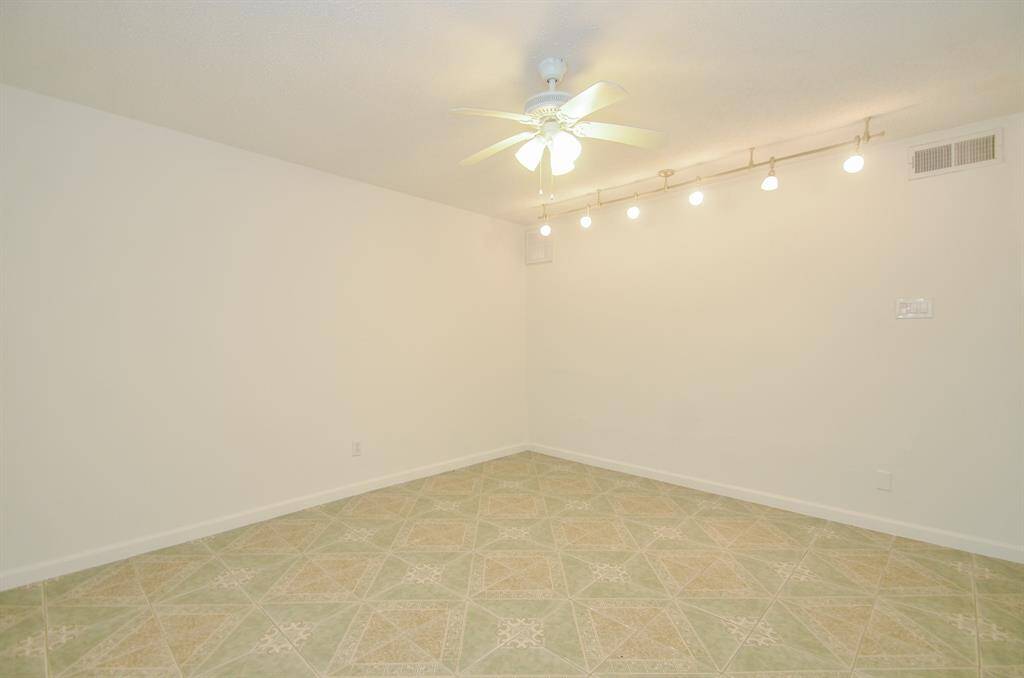 This room features neutral walls, patterned tile flooring, a ceiling fan, and track lighting, offering a versatile space for various uses in the home.