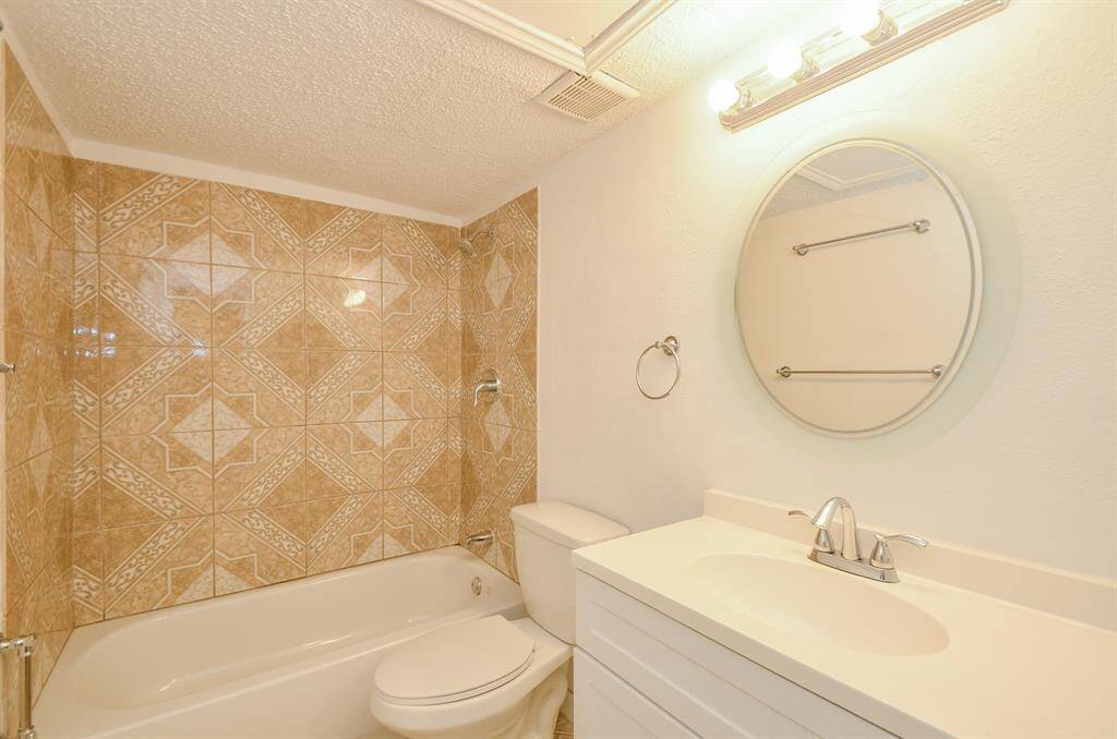 Bright bathroom with patterned tile walls, a bathtub, and a modern vanity featuring a round mirror and sleek lighting.
