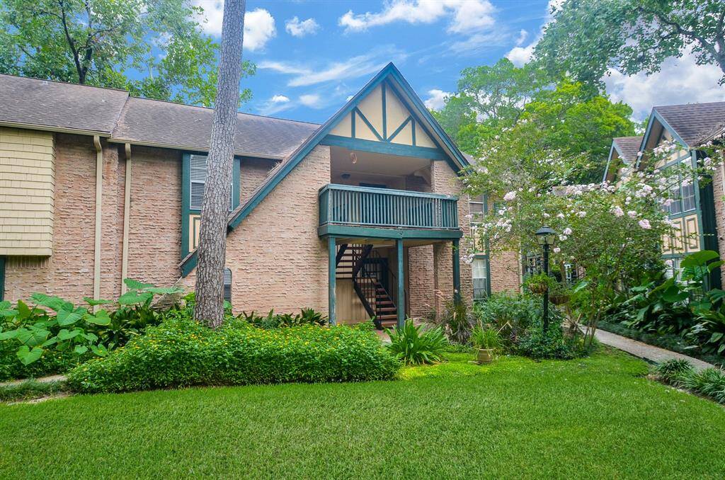 Charming two-story home with Tudor-style accents, featuring a brick exterior and a balcony. Surrounded by lush greenery and mature trees, it offers a peaceful, inviting atmosphere.