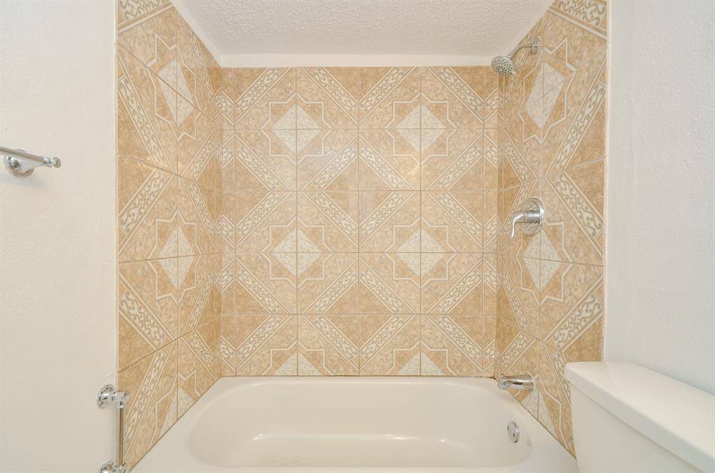 This bathroom features a tiled shower/bathtub combo with intricate beige and white patterns, offering a classic and clean look.