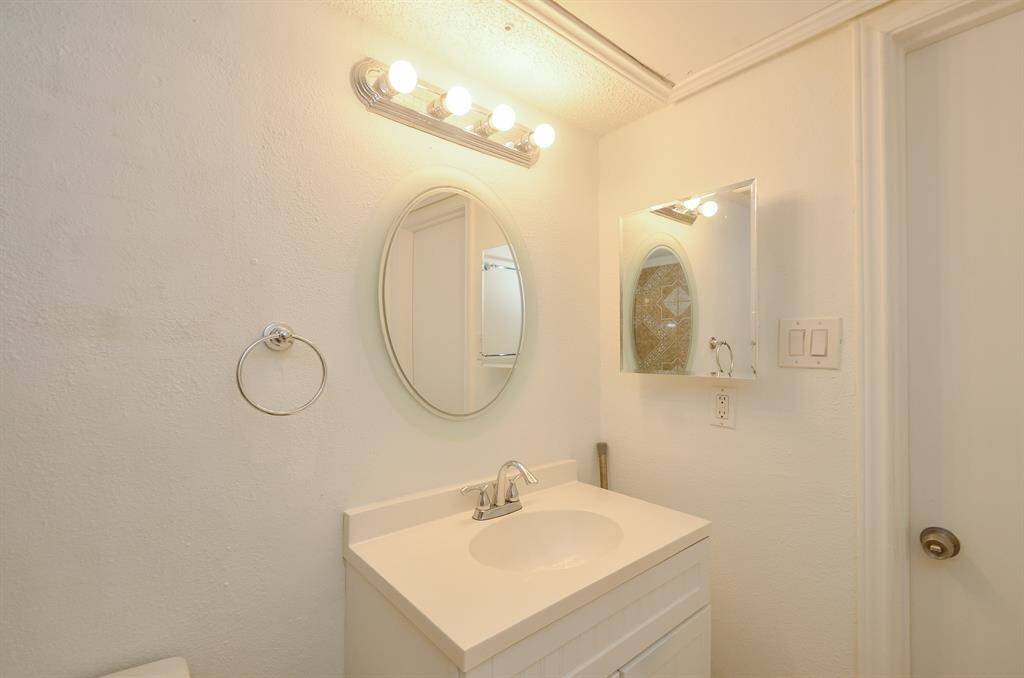 This bathroom features a clean, minimalist design with a white vanity, oval mirror, and bright vanity lighting. The neutral tones create a fresh and inviting atmosphere.