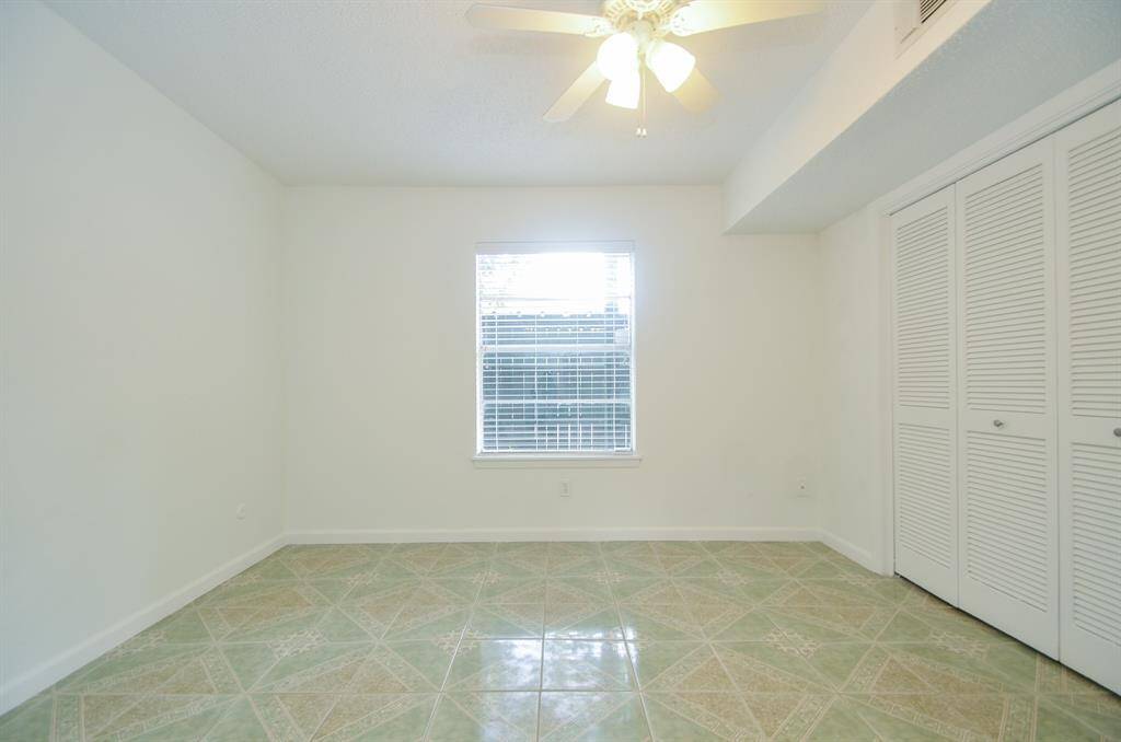 Bright room with tiled flooring, a ceiling fan, and a window providing natural light. Features include a large closet with louvered doors.