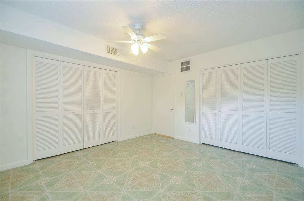 This room features ample closet space with multiple white louvered doors, a ceiling fan for comfort, and light-colored tiled flooring, creating a bright and airy atmosphere.