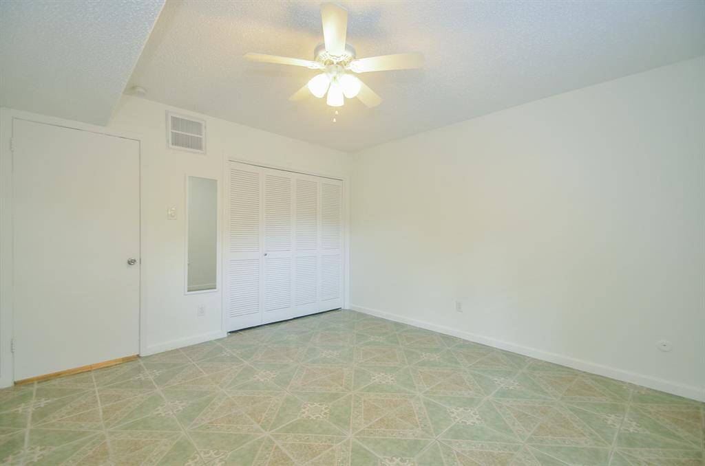 This room features a ceiling fan, light-colored walls, and a patterned floor. There's a closet with louvered doors and a small mirror on the wall, providing a clean and simple space.
