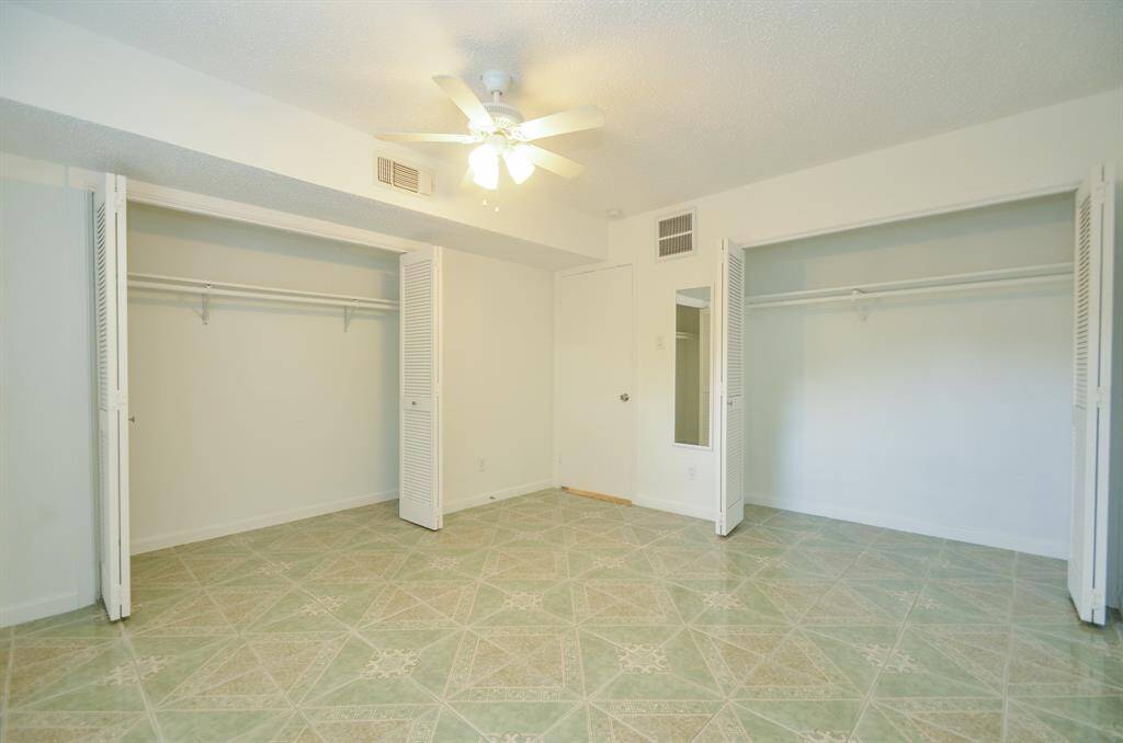 This room features two spacious closets with louvered doors, a ceiling fan, and patterned tile flooring, offering ample storage and a comfortable atmosphere.
