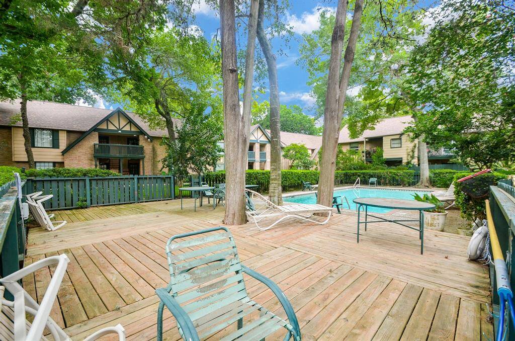 Charming property featuring a spacious wooden deck with seating, overlooking a serene pool area. Surrounded by lush trees and attractive townhouse-style buildings, offering a tranquil and inviting atmosphere. Perfect for relaxation and outdoor enjoyment.
