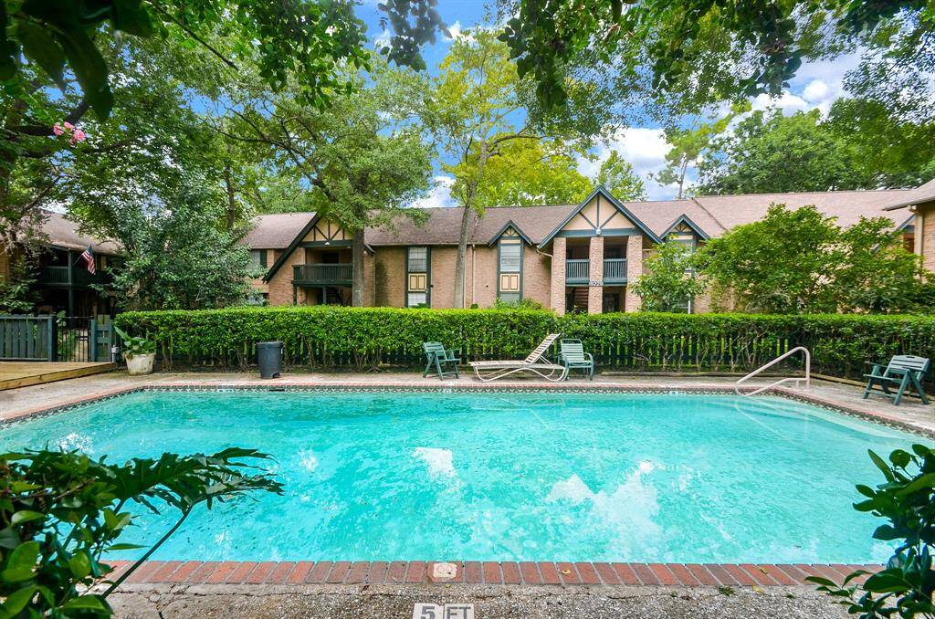 This photo showcases a charming residential area with a refreshing swimming pool surrounded by lush greenery. The backdrop features Tudor-style townhouses, offering a serene and inviting atmosphere. Perfect for relaxation and community living.