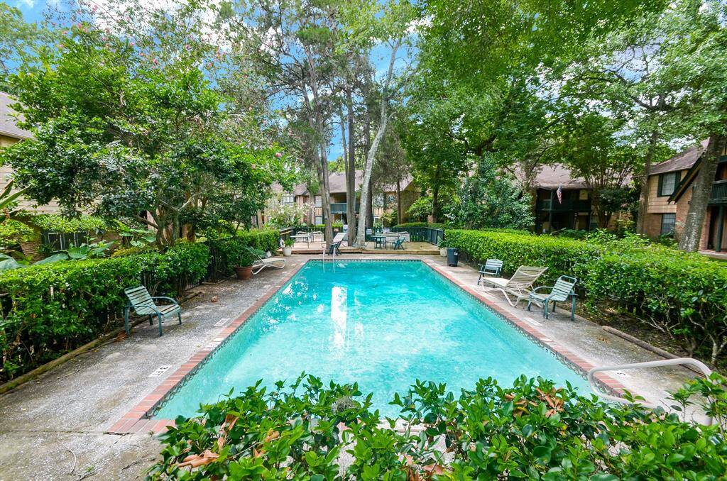 This photo showcases a serene outdoor area featuring a rectangular swimming pool surrounded by lush greenery and trees. There are lounge chairs and a paved deck, providing a relaxing environment. The setting is peaceful, offering a private, natural retreat.