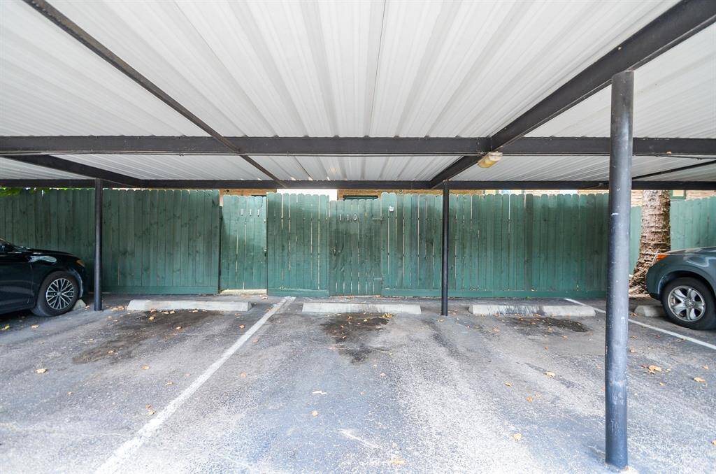 This photo shows a covered parking area with ample space for vehicles, featuring a sturdy metal roof and a wooden fence for privacy.