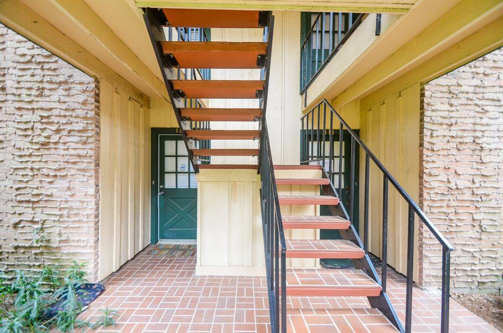 This photo showcases a rustic outdoor stairway with metal railings leading to an upper level. The area features a brick-patterned floor and textured walls, providing a cozy and inviting entrance.