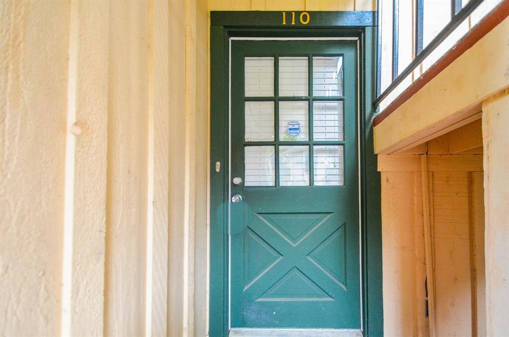 The photo shows a cozy entryway with a green door featuring a grid of windows. The door is numbered "110" and is set in a light-colored, textured wall, creating a warm and inviting entrance.