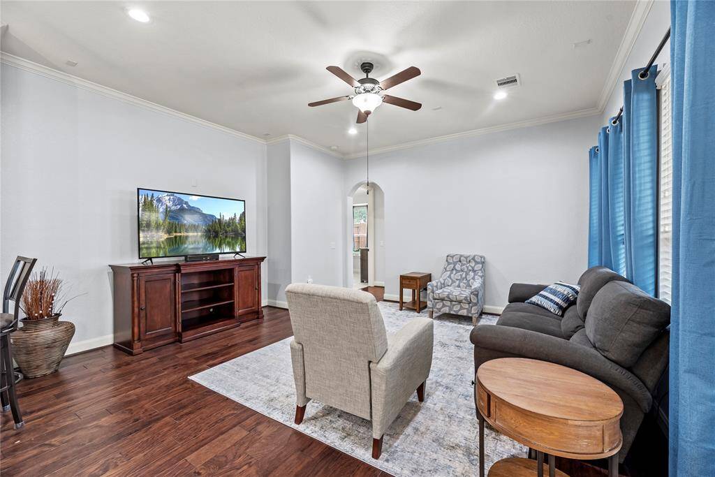The family room is an inviting space to relax and unwind, featuring engineered wood flooring, fresh neutral paint, crown molding, and elegant arched doorways. Oversized windows fill the room with natural light, while a raised ceiling with recessed lights and a lit fan adds to the open and airy ambiance.