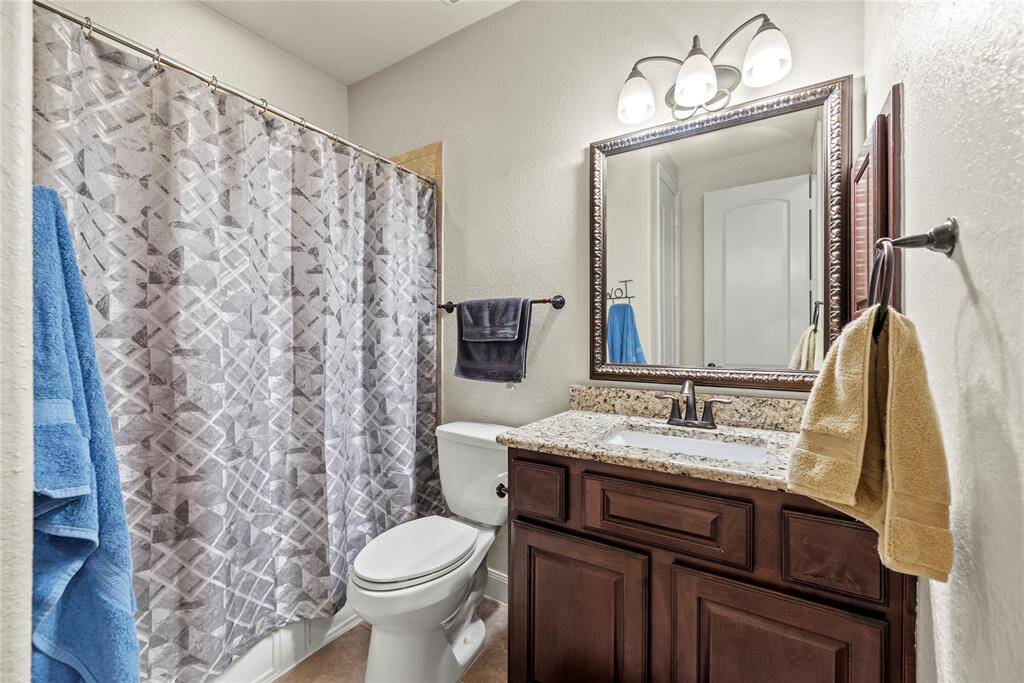 This full bathroom offers both style and functionality, featuring a single sink vanity with a sleek granite countertop, a framed mirror with coordinating vanity lights above, and a built-in medicine cabinet for extra storage. You'll also find a fully tiled tub/shower enclosure.