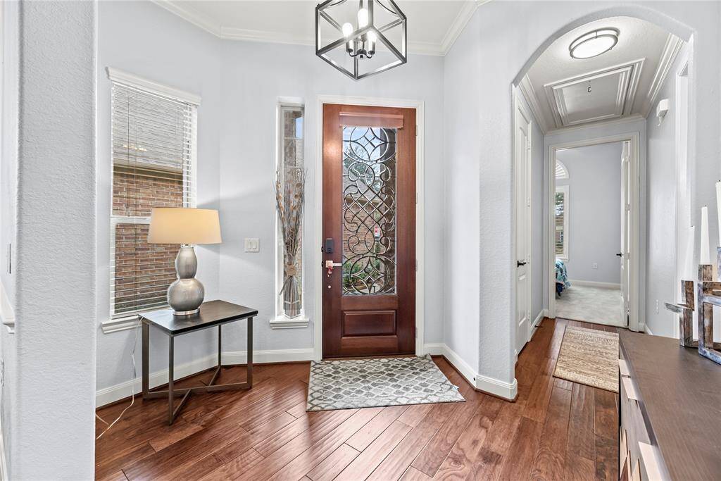 The foyer makes a lasting first impression with an elegant leaded glass door, engineered wood flooring, neutral paint, arched doorways, and raised ceilings with crown molding and chic lighting.