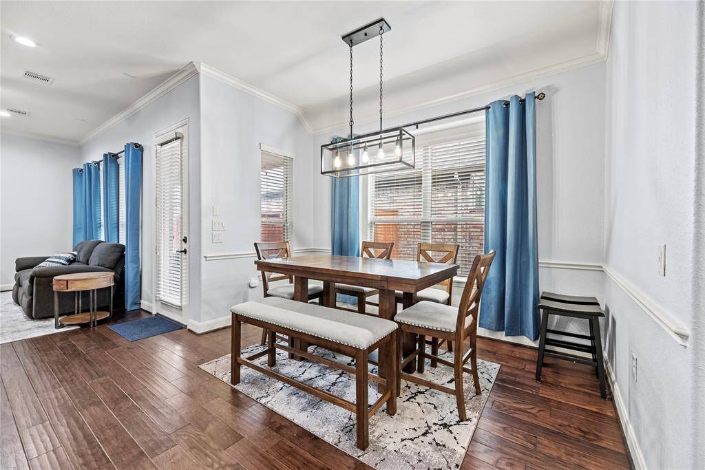 This open dining room provides the ideal setting for lavish dinner parties and casual gatherings, featuring gorgeous engineered wood flooring, neutral paint, chair rail and crown moldings, and oversized windows that fill the space with natural light. An eye-catching chandelier enhances the ambiance, perfectly blending timeless elegance with modern farmhouse charm.