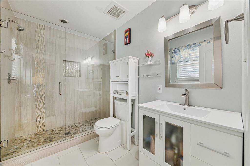 The ensuite primary bathroom has a large shower with gleaming tile and a seamless shower door. The vanity has drawer and cabinet storage with a one piece countertop and sink with brushed nickel faucet.
