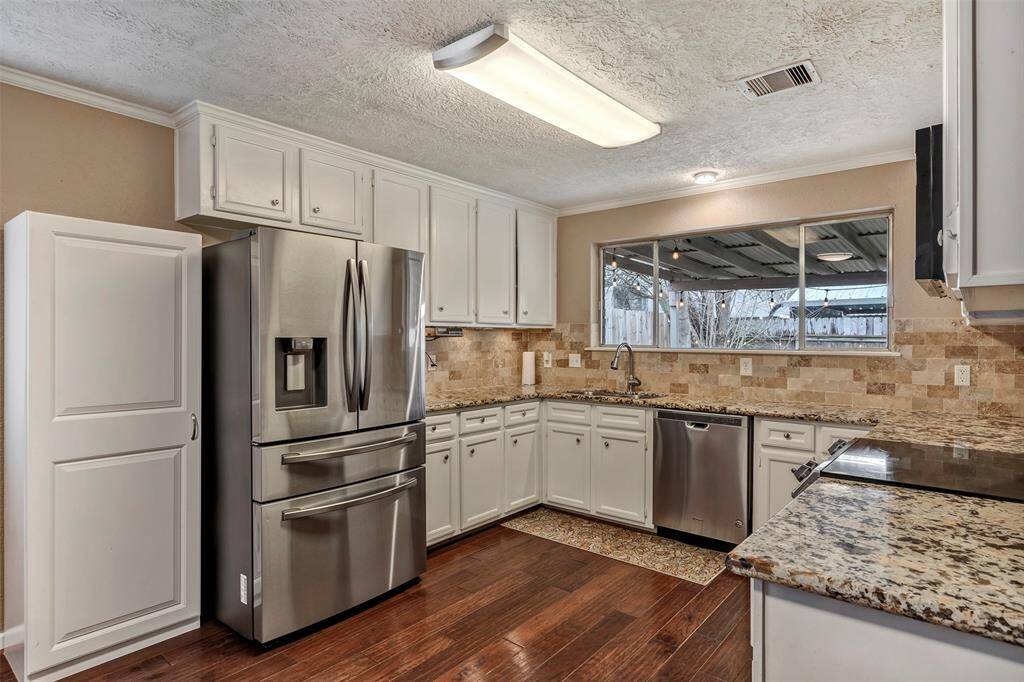 This kitchen features stainless steel appliances, granite countertops, and ample cabinet space. It has a large window providing natural light and a view of the backyard.