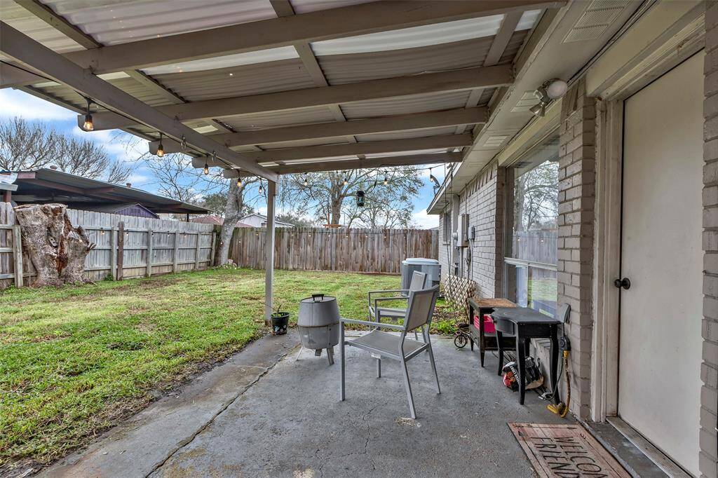 This photo showcases a backyard with a covered patio area, perfect for outdoor gatherings. The yard is fenced, providing privacy, and features a mix of grass and mature trees. It's an inviting space for relaxation and entertainment.