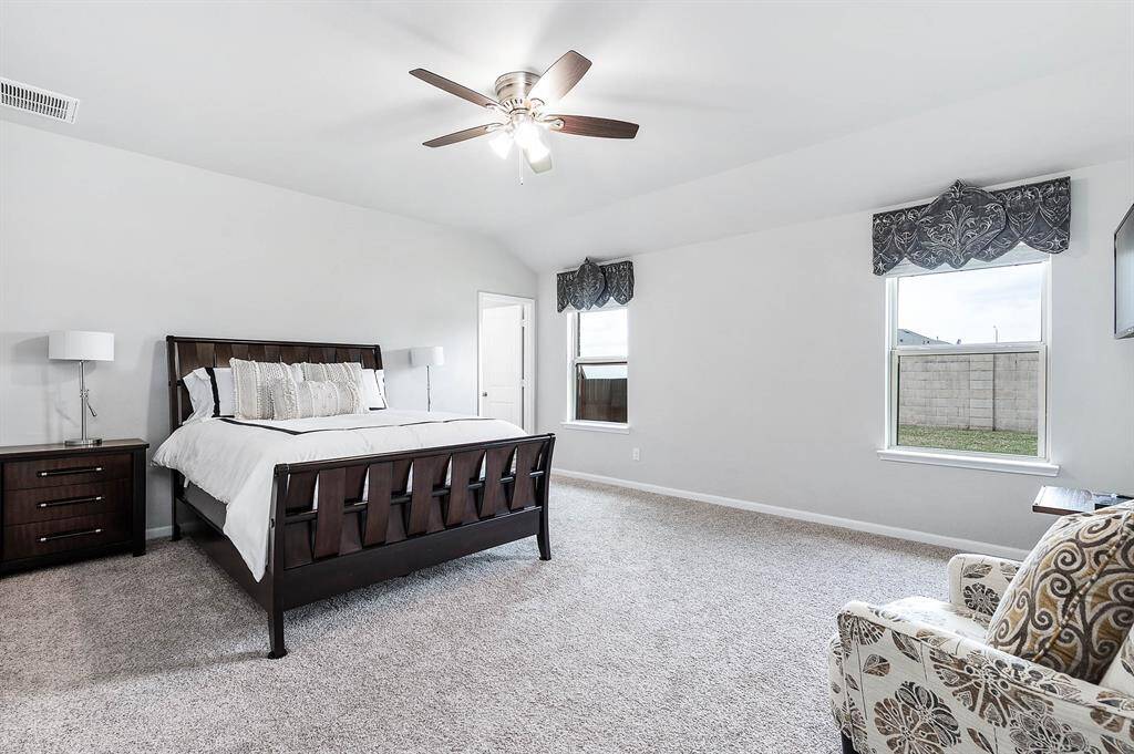 This spacious Primary bedroom features a spa-like en-suite bathroom, plush carpeting, and ample natural light from two windows.
