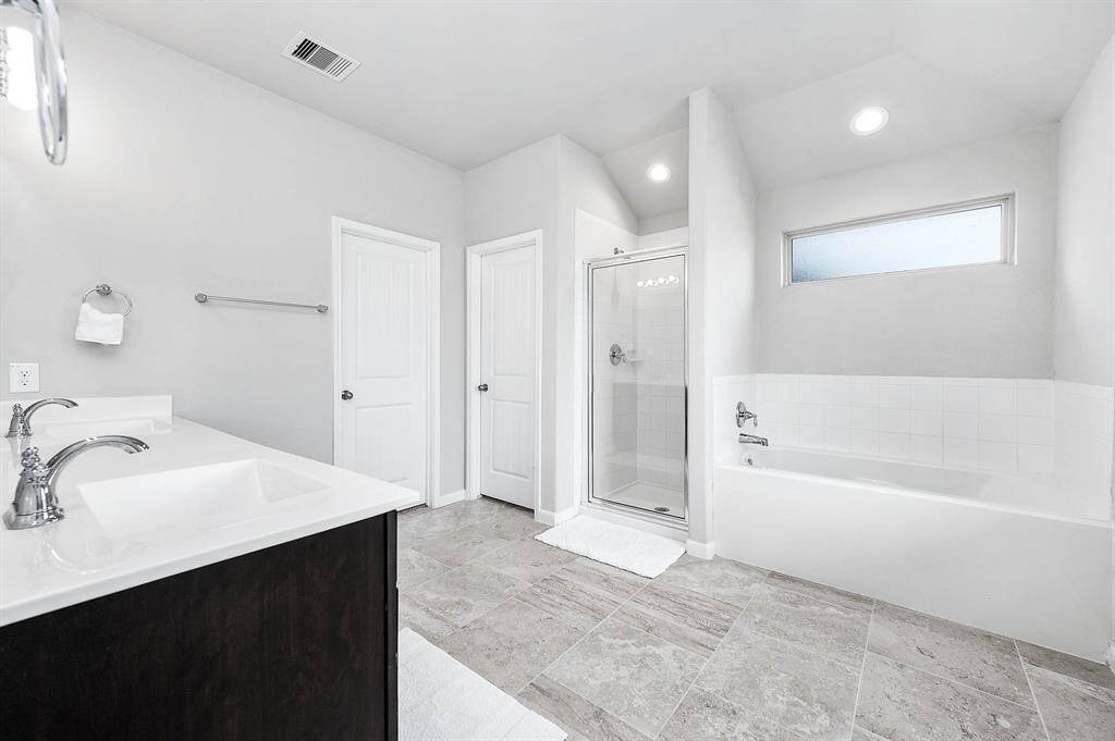 This spacious, modern bathroom features a sleek double vanity, a glass-enclosed shower, and a separate bathtub. With neutral tile flooring and soft lighting, it offers a clean and inviting atmosphere.