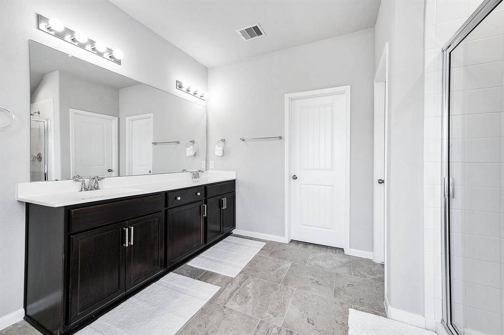 This spacious, modern bathroom features a sleek double vanity, a glass-enclosed shower, and a separate bathtub. With neutral tile flooring and soft lighting, it offers a clean and inviting atmosphere.