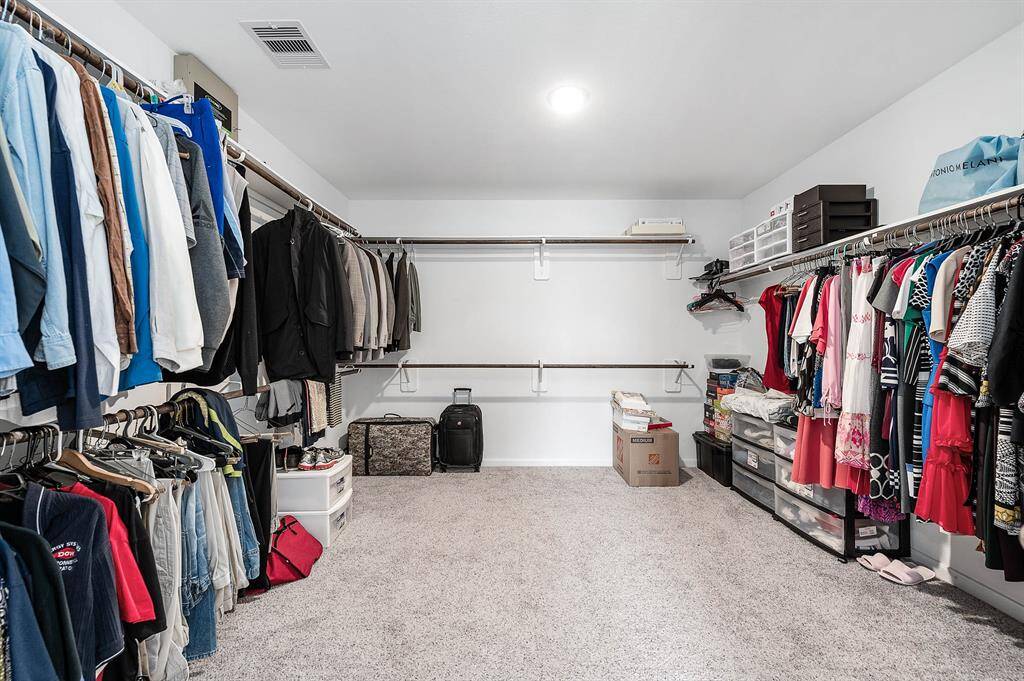 This spacious walk-in closet features ample hanging space on both sides, built-in shelves for organization, and a carpeted floor. Ideal for extensive wardrobes or extra storage.
