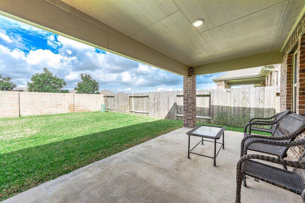 A cozy covered patio with seating, overlooking a spacious fenced backyard, perfect for outdoor relaxation and entertainment.