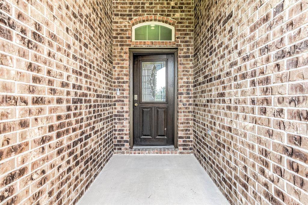 A welcoming entryway with a brick exterior leads to a sturdy wooden front door featuring decorative glass, offering both security and style.