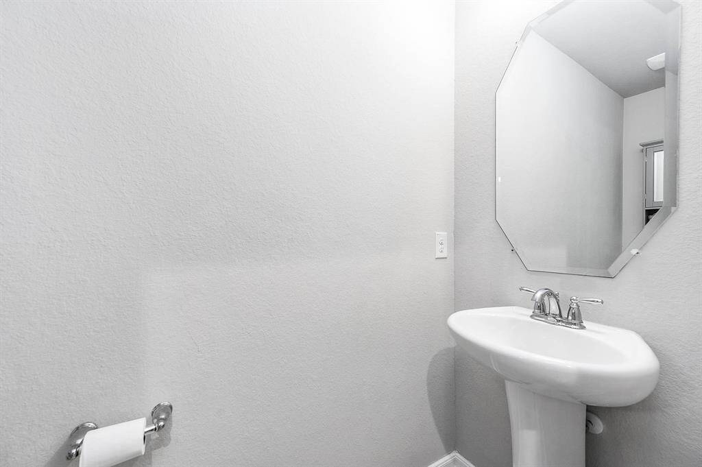 A modern half-bathroom featuring a pedestal sink, geometric mirror, and neutral gray walls.