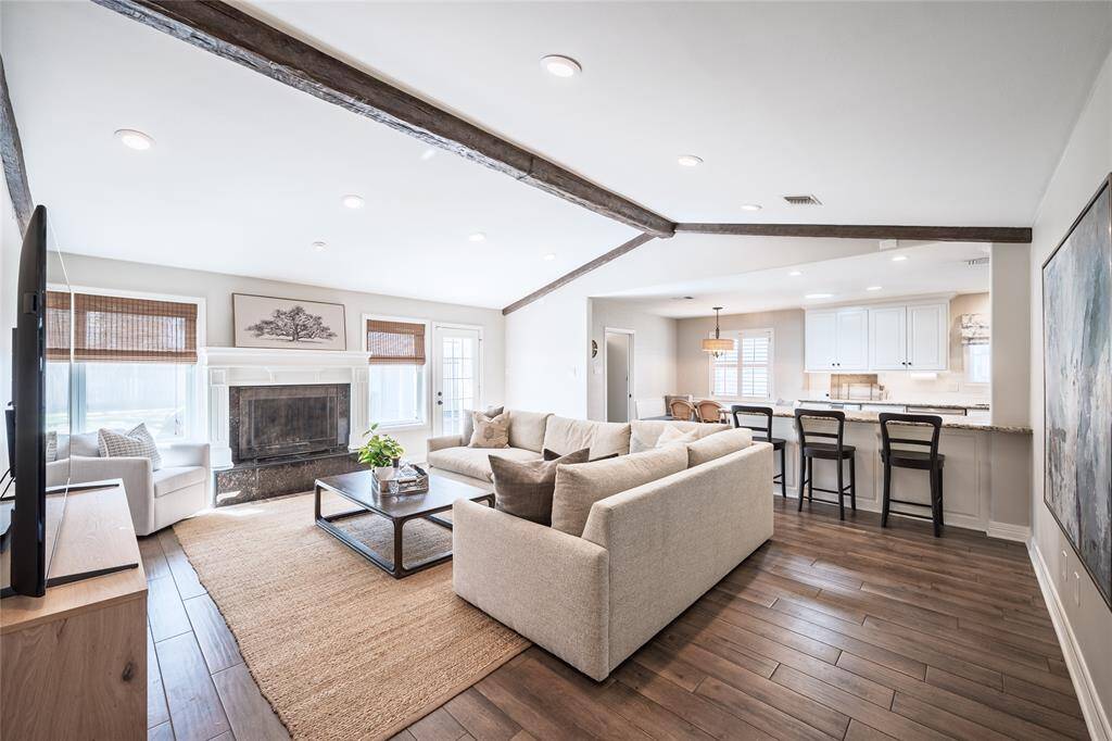 Living room offers an abundance of natural light, gas log fireplace, and a crisp, neutral color palette. Classic beams and wood-tile flooring complete the design.